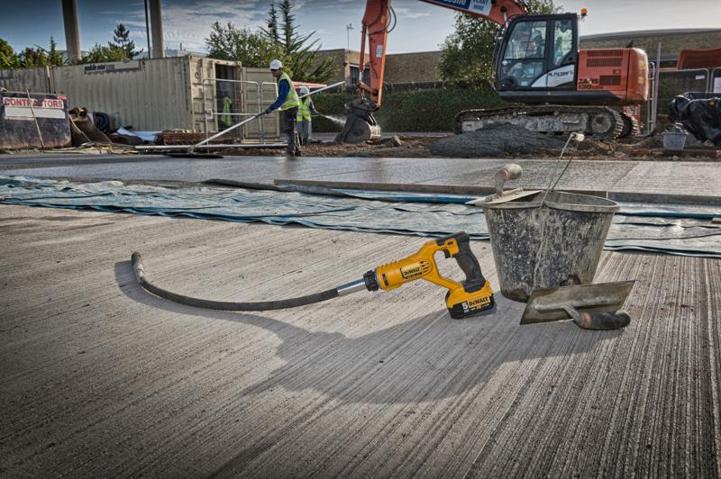 DEWALT Akku-Gerät auf Beton mit Eimer und Kelle. Bauarbeiter und Bagger im Hintergrund.